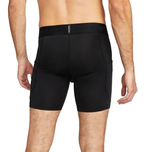 En person står og kigger væk fra kameraet iført Nike Pro Dri-FIT Fitness Shorts, Herre, Black/White med en synlig linning med mærke. De mellemlange shorts dækker lårene, og baggrunden er helt hvid.