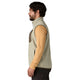 En mand med mørkt hår og skæg, iført en Patagonia R1 Air Vest, Herre, Pelican – en let og åndbar fleecevest til mænd – i beige over en lysebrun langærmet skjorte og mørke bukser, står i profil med ansigtet vendt mod venstre foran en hvid baggrund.