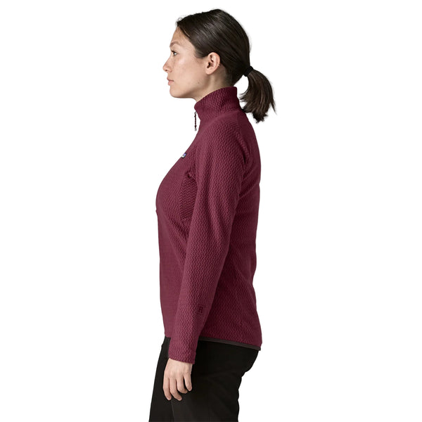 En kvinde set i profil iført en mørkerød Patagonia R1 Air Zip Neck i farven Berry Fig, en pullover med lynlås i halsen og et struktureret chevronmønster.
