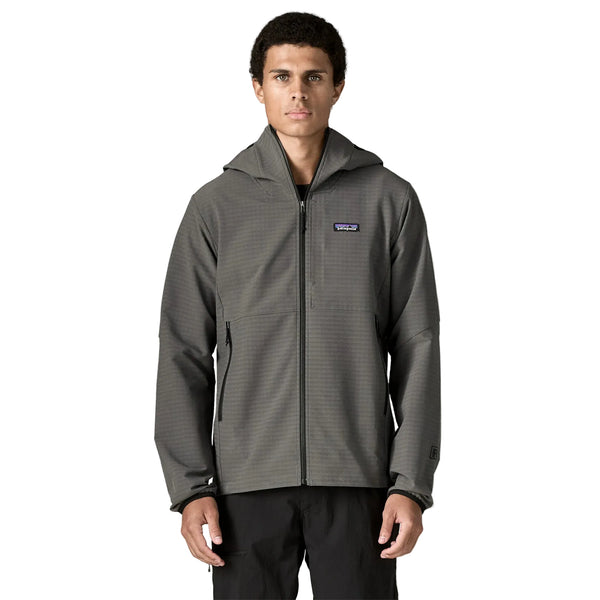 En person står med ansigtet vendt fremad og er iført en Patagonia R1 TechFace Hoody, Herre, i farven Forge Grey samt sorte bukser. Hoodien har et lille rektangulært Patagonia-logo på venstre bryst. Baggrunden er ensfarvet hvid.