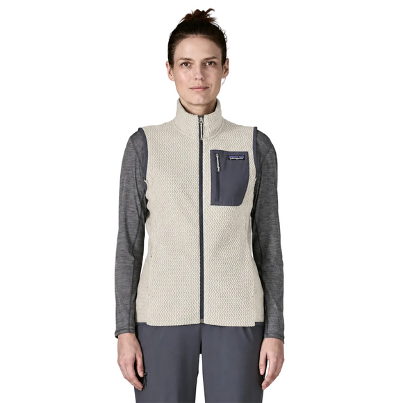 En person iført en Patagonia R1 Air Vest, Dame i farven Birch White, med en grå brystlomme med lynlås, over en grå langærmet skjorte, stående foran en ensfarvet hvid baggrund.