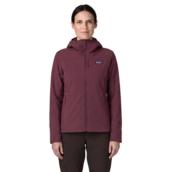 En person står med ansigtet vendt fremad iført en Patagonia R1 CrossStrata-hoodie til kvinder i farven Berry Fig og sorte bukser. Hoodien har en hætte og et lille Patagonia-logo på venstre bryst. Baggrunden er ensfarvet hvid.