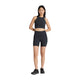 En kvinde med glat mørkt hår og et neutralt udtryk står med front mod en almindelig hvid baggrund iført en sort New Balance-atletiktop, RC Elite Storage Short 6" Dame i sort og sorte atletiksko.