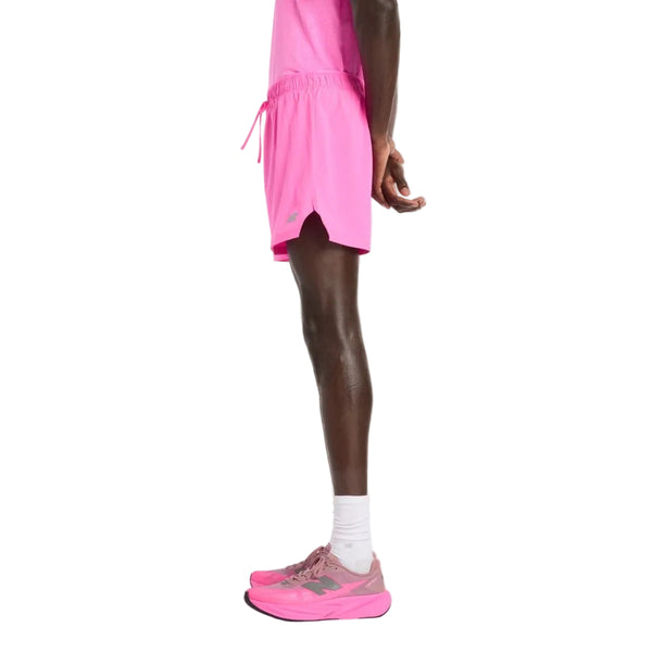 En person står i profil mod en almindelig hvid baggrund iført New Balance RC Short 5" Herre i Pink Heat, en matchende T-shirt, hvide sokker og lyserøde sportssko. Hænderne er bag ryggen, klar til løbetræning.
