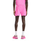 En person står med ryggen til kameraet iført en lyserød skjorte, New Balance RC Short 5" Herre in Pink Heat, hvide sokker og lyserøde sportssko på en almindelig hvid baggrund.