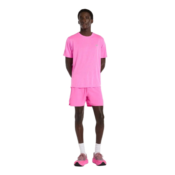 En person står med front mod en almindelig hvid baggrund iført en lyserød T-shirt, New Balance RC Short 5" Herre Pink Heat, hvide sokker og lyserøde sneakers.
