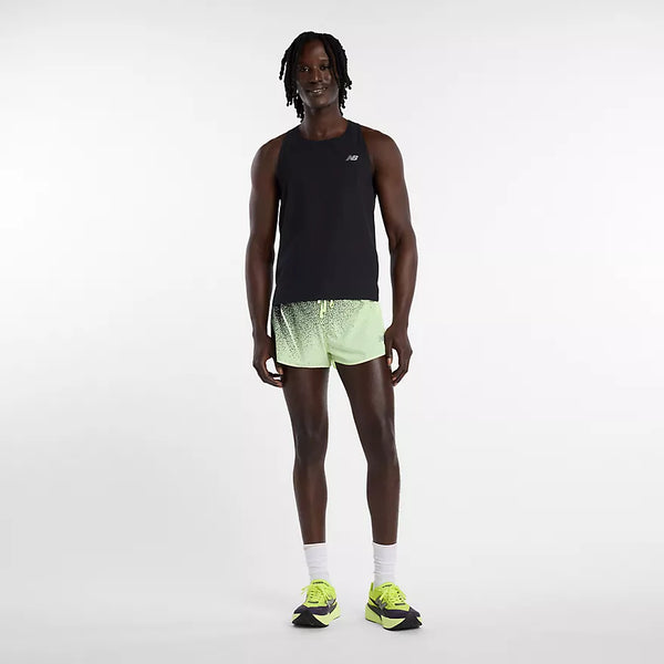 En person står på en almindelig lys baggrund iført en sort ærmeløs sportstop, New Balance RC Ultra Light Printed Short 3" Herre Afterglow, hvide sokker og neongule løbesko.