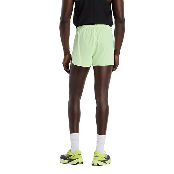 En person vender ansigtet væk iført en sort ærmeløs top, New Balance RC Ultra Light Printed Short 3" Herre in Afterglow, hvide strømper og lysegrønne/grå sportssko, fotograferet mod en almindelig hvid baggrund.