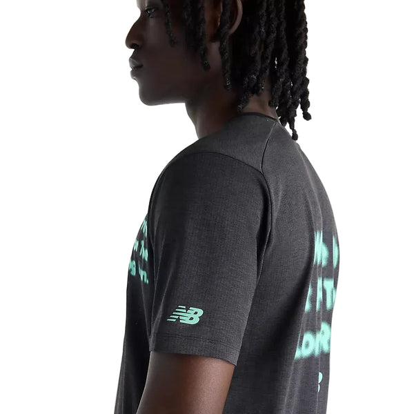 En person med mellem-mørk hud og skulderlange twists ses set fra siden iført New Balance RC Essential Graphic T-shirt til mænd i farven Black/Bright Mint. Denne herre-trænings-T-shirt har et lille logo på ærmet, et diskret tekstdesign i farven teal på ryggen samt åndbart mesh, der sikrer øget komfort under enhver træning.