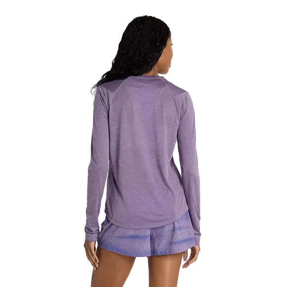 En person med langt krøllet hår, set bagfra mod en hvid baggrund, er iført New Balance Athletics Long Sleeve Dame top i Candied Violet Heather og lyslilla mønstrede shorts.