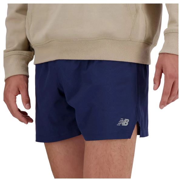 En person er iført en beige sweatshirt og New Balance RC Short 5" herre i navy/saltgrå, vist fra taljen til midt på låret med armene afslappet i siden.
