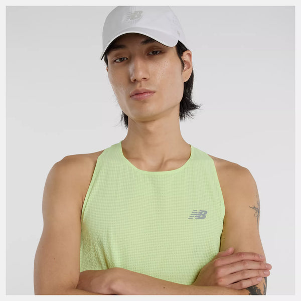 En person iført en hvid New Balance-kasket og New Balance Race Day Ultra Light Singlet, Herre, Afterglow står med armene over kors på en almindelig baggrund.