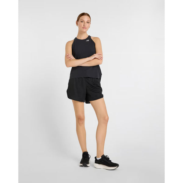 En kvinde står på en ensfarvet baggrund iført sort New Balance Race Day Ultra Light Singlet, Dame, sorte shorts og løbesko. Løbesinglettens NB ICE-teknologi sikrer overlegen komfort til langdistanceløb.