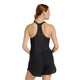 En kvinde med lys hud og brunt hår i en lav hestehale ses bagfra iført New Balance Race Day Ultra Light Singlet, Dame, Black og sorte sportsshorts på en almindelig hvid baggrund.