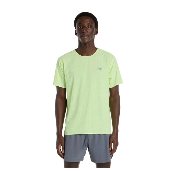 En mand står og kigger fremad i en lysegrøn New Balance Race Day Ultra Light T-Shirt, Herre, Afterglow med NB ICEx-teknologi og grå sportsshorts, perfect løbetøj herre, mod en almindelig hvid baggrund.