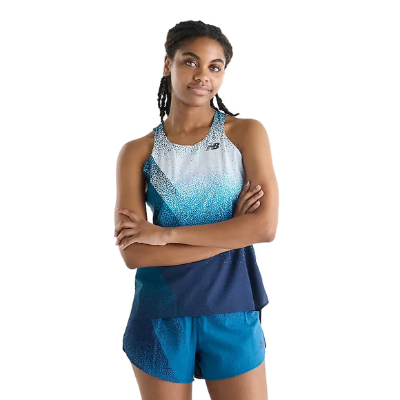 En kvinde med mellemlangt, flettet hår står med armene over kors og har en New Balance Race Day Ultra Light Printed Singlet, Dame, Altitude samt matchende blå shorts fra Race Day-kollektionen på. Hun poserer foran en ensfarvet hvid baggrund.