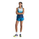 En person står med armene over kors og har en ærmeløs, blå New Balance Race Day Ultra Light Printed Singlet til kvinder i farvekombinationen »Altitude« på, samt matchende blå shorts, hvide sokker og farverige New Balance-løbesko. Baggrunden er ensfarvet hvid.
