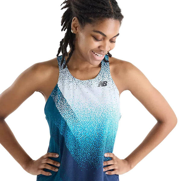 En person med mørkt, flettet hår smiler og kigger ned, mens hun har New Balance Race Day Ultra Light Printed Singlet til kvinder i farvekombinationen »Altitude« på. Denne ærmeløse, blå og hvide sportstop er prydet med det karakteristiske New Balance-logo og er udstyret med NB ICE-teknologi, der sikrer komfort under intensive træningspas. Baggrunden er ensfarvet hvid.