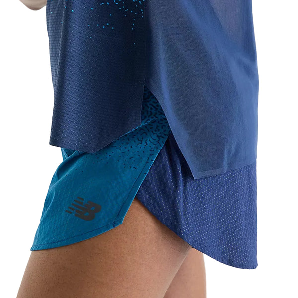 Et nærbillede af en person iført blå sportsshorts og en matchende blå New Balance Race Day Ultra Light Printed Singlet, Dame, Altitude. Shortsene har et sort New Balance-logo tæt på sømmen, mens den innovative NB ICE-teknologi sikrer optimal komfort. Baggrunden er ensfarvet hvid.