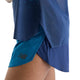 Et nærbillede af en person iført blå sportsshorts og en matchende blå New Balance Race Day Ultra Light Printed Singlet, Dame, Altitude. Shortsene har et sort New Balance-logo tæt på sømmen, mens den innovative NB ICE-teknologi sikrer optimal komfort. Baggrunden er ensfarvet hvid.