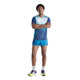 En mand står med armene over kors og har en New Balance Race Day Ultra Light Printed T-shirt, Herre, Altitude på – kombineret med matchende blå shorts, grå sokker og neonfarvede løbesko. Baggrunden er helt hvid.