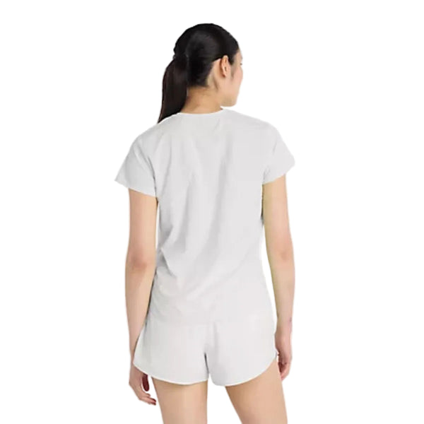 En kvinde med langt mørkt hår i hestehale ser væk fra kameraet og er iført New Balance Race Day Ultra Light T-Shirt, Dame, i Grey Matter. Hun står på en almindelig hvid baggrund.