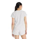 En kvinde med langt mørkt hår i hestehale ser væk fra kameraet og er iført New Balance Race Day Ultra Light T-Shirt, Dame, i Grey Matter. Hun står på en almindelig hvid baggrund.