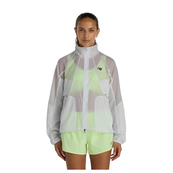 En person står og kigger fremad iført en gennemsigtig grå New Balance Rc Jacket, Dame over en neongrøn sports-bh og matchende shorts. Dette sporty look er perfekt til en aktiv dag, og den ensfarvede hvide baggrund fremhæver outfittet.