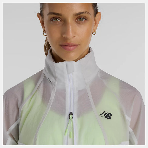 En person med lysebrunt hår, der er trukket tilbage, er iført New Balance Rc Jacket, Dame, Grey, med høj krave, lynlås foran og New Balance-logo på venstre side. Baggrunden er ensfarvet og lysegrå.