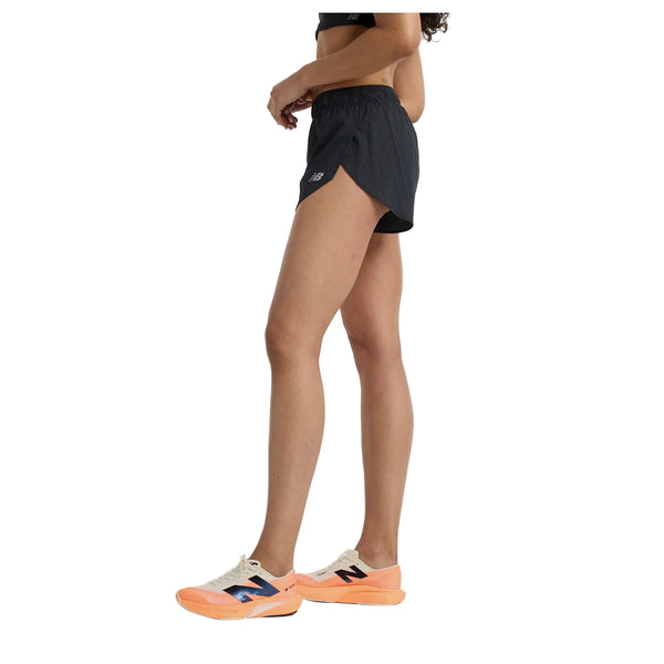 En person står i profil iført en sort sports-bh, New Balance Rc Ultra Light Split Short 3" Dame i sort og hvide løbesko med orange såler på en hvid baggrund.