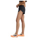 En person står i profil iført en sort sports-bh, New Balance Rc Ultra Light Split Short 3" Dame i sort og hvide løbesko med orange såler på en hvid baggrund.