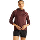 En person står med ansigtet vendt fremad iført New Balance Rc Essential Heat Grid Hoodie, Dame, i farven Cherry Leather med NB HEAT-teknologi og sorte sportsshorts foran en ensfarvet hvid baggrund – perfekt til løb i koldt vejr.