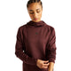 En kvinde iført en Cherry Leather New Balance RC Essential Heat Grid-hoodie med NB HEAT-teknologi kigger ned, mens hun retter på ærmet – perfekt til løb i koldt vejr. Baggrunden er ensfarvet hvid.