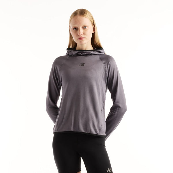 En person har en grå New Balance Rc Essential Heat Grid-hoodie med gittermønster på, Dame, Neptune Grey, på sammen med sorte leggings.
