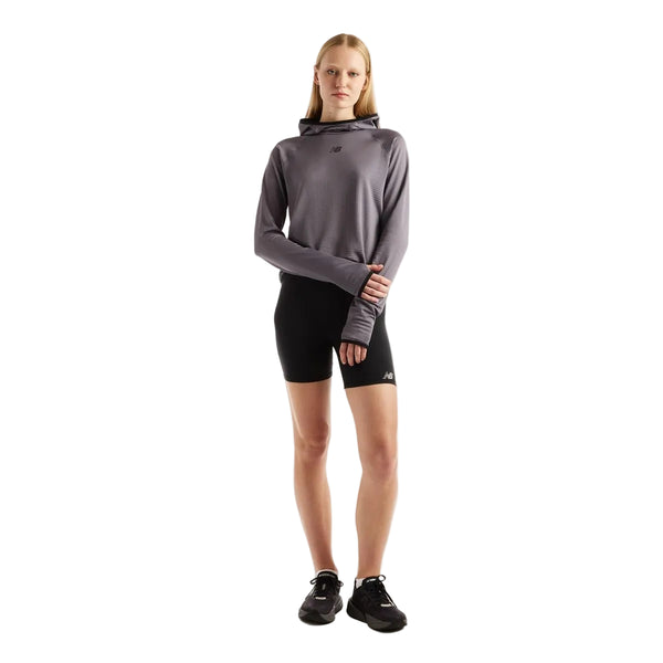 En kvinde iført en New Balance Rc Essential Heat Grid-hoodie i farven Neptune Grey med tommelfingerhuller, sorte sportsshorts og sorte sneakers.