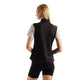 Der ses et billede bagfra af en person med glat, langt blondt hår, der bærer en sort New Balance Rc Essential Heat Grid-vest til kvinder over en lys kortærmet skjorte og sorte, tætsiddende shorts, mens vedkommende står foran en ensfarvet hvid baggrund.