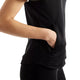 En person, der bærer den sorte Rc Essential Heat Grid-vest fra New Balance, stikker sin højre hånd ned i en sidelomme med lynlås på vesten, hvilket fremhæver dens elegante og funktionelle design. Kun den øverste del af overkroppen og armen er synlige på en hvid baggrund.