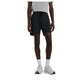 En person iført en grå T-shirt, hvide sokker, hvide sneakers og et par New Balance Rc Essential Short 7" (Herre, sort) står foran en hvid baggrund. Personens hoved er ikke synligt på billedet.