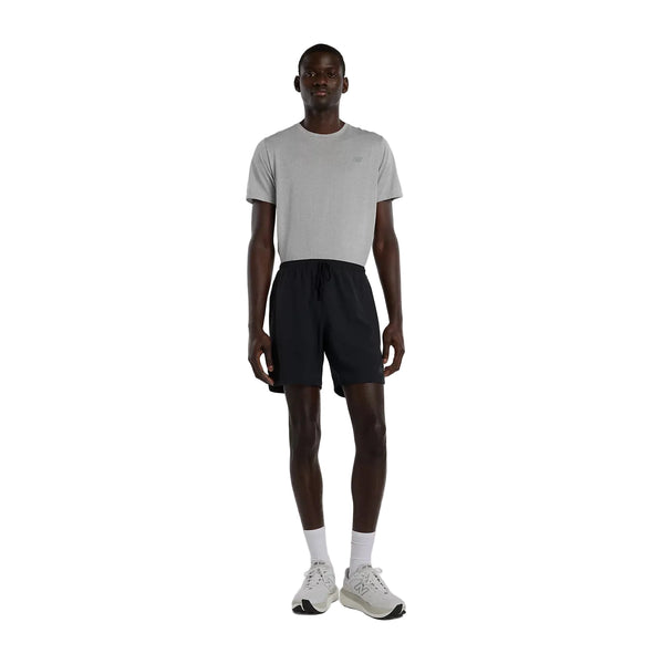 En mand står vendt fremad iført en lysegrå T-shirt med korte ærmer, et par New Balance Rc Essential Short 7" til mænd i sort, hvide strømper og hvide sportssko foran en ensfarvet hvid baggrund.