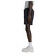 En person set i profil er iført en grå T-shirt, sorte New Balance Rc Essential Short 7" (Herre), hvide ankelstrømper og hvide sportssko foran en ensfarvet hvid baggrund.