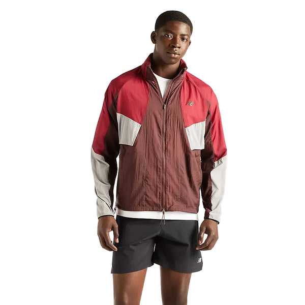 En mand iført en New Balance RC-jakke i kirsebærrødt læder til mænd – en sporty, vandafvisende jakke – kombineret med sorte shorts står med ansigtet vendt fremad foran en hvid baggrund.