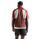 En person står med ryggen til og har den elegante New Balance Rc-jakke til mænd i farven »Cherry Leather« på – en løbejakke i farvekombinationen maroon, rød og grå – samt sorte shorts. Baggrunden er helt hvid.