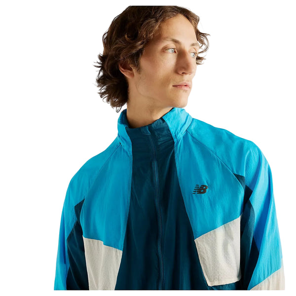 En mand med bølget brunt hår har en blå og hvid New Balance Rc-jakke på – Herre, Streamsong – en let og vandafvisende jakke. Han kigger til siden foran en ensfarvet hvid baggrund.