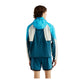 Der ses en person med mellemlangt brunt hår set bagfra, iført en blå og hvid New Balance Rc-jakke, Herre, Streamsong, med matchende shorts. Jakken er vandafvisende. Baggrunden er hvid.