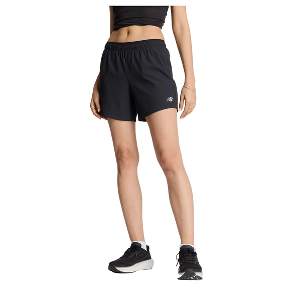 En person iført en sort crop top, et par sorte New Balance Rc Short 5" Dame-shorts og sorte løbesko står foran en hvid baggrund. Personens hoved kan ikke ses på billedet.