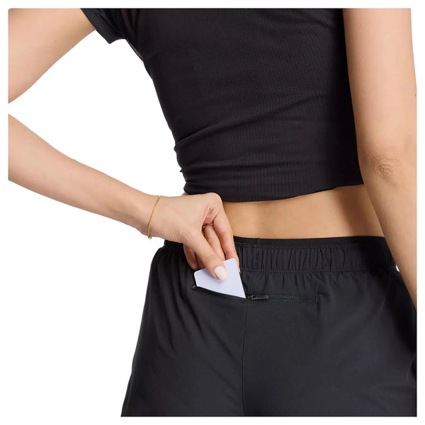 En person iført New Balance Rc Short 5", Dame, Sort er i færd med at lægge et kort i lommen med lynlås i linningen på disse svedtransporterende løbeshorts, mens vedkommende har en sort top på.