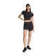 En person står foran en hvid baggrund iført en sort kasket, en sort kortærmet crop-top, et par New Balance Rc Short 5" Dame i sort og sorte sneakers, med den ene hånd på hoften.