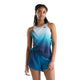En kvinde står foran en hvid baggrund iført en blå og hvid ombre-trænings-tanktop og matchende New Balance Rc Ultra Light Printed Short 3″ i farven Altitude. Hun har hånden hvilende på hoften og kigger let til siden, hvilket fremhæver de åndbare løbeshorts fra New Balance, der er perfekte til den aktive kvinde.