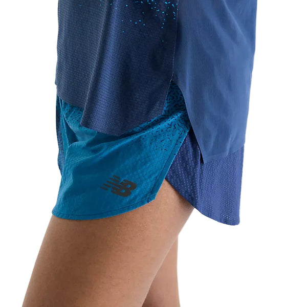 Et nærbillede af en person, der bærer blå New Balance Rc Ultra Light Printed Short 3″, Dame, Altitude, kombineret med en matchende blå top. Kun underkroppen og lårene er synlige på en hvid baggrund, hvilket fremhæver det elegante design af disse ultralette løbeshorts til kvinder.