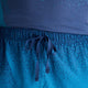 Nærbillede af en person, der bærer New Balance Rc Ultra Light Printed Short 3″, Herre, Altitude med elastisk linning og snøre, der kan bindes, over en blå skjorte med struktur.
